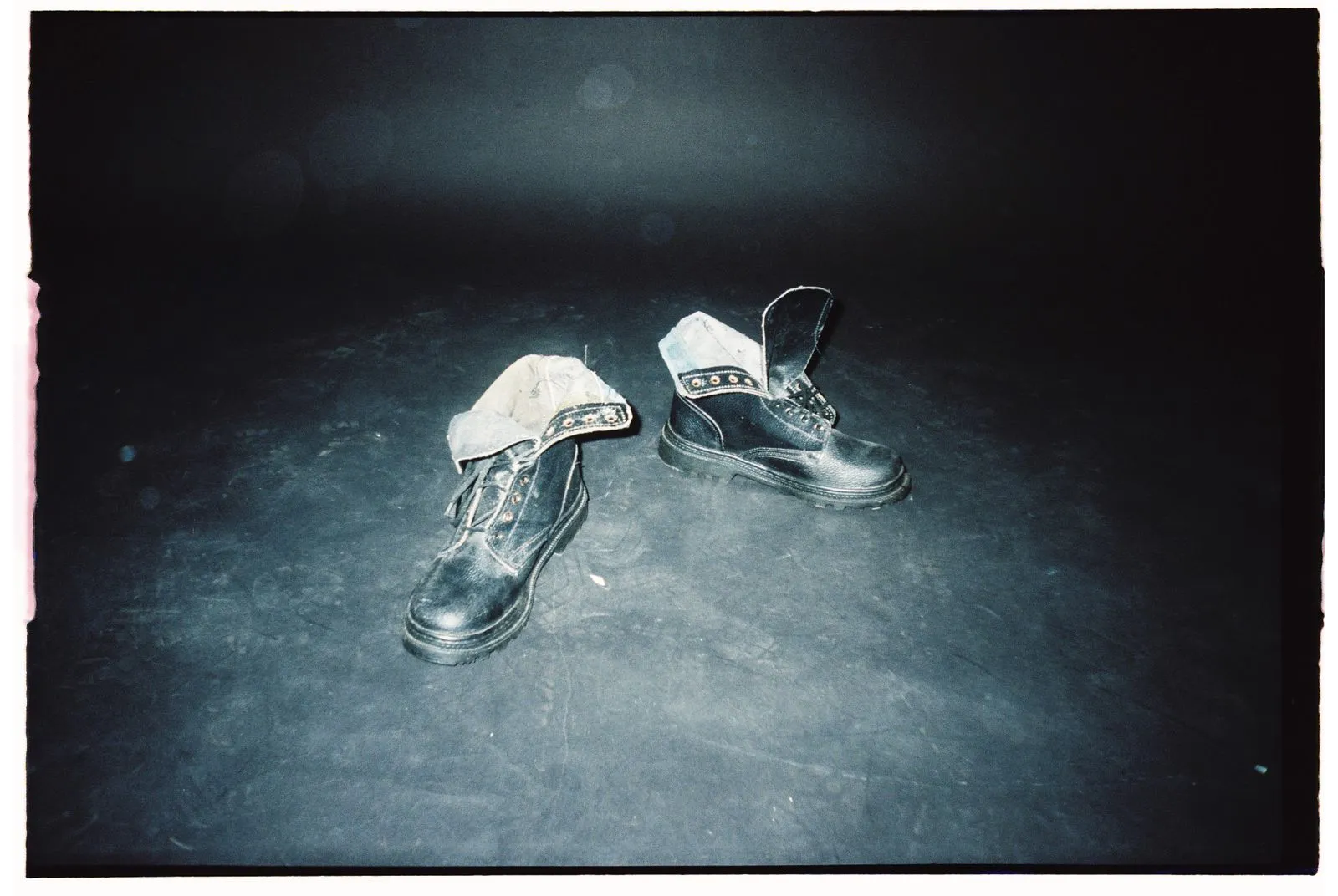 Close-up of black leather boots on a dusty floor under spotlight.